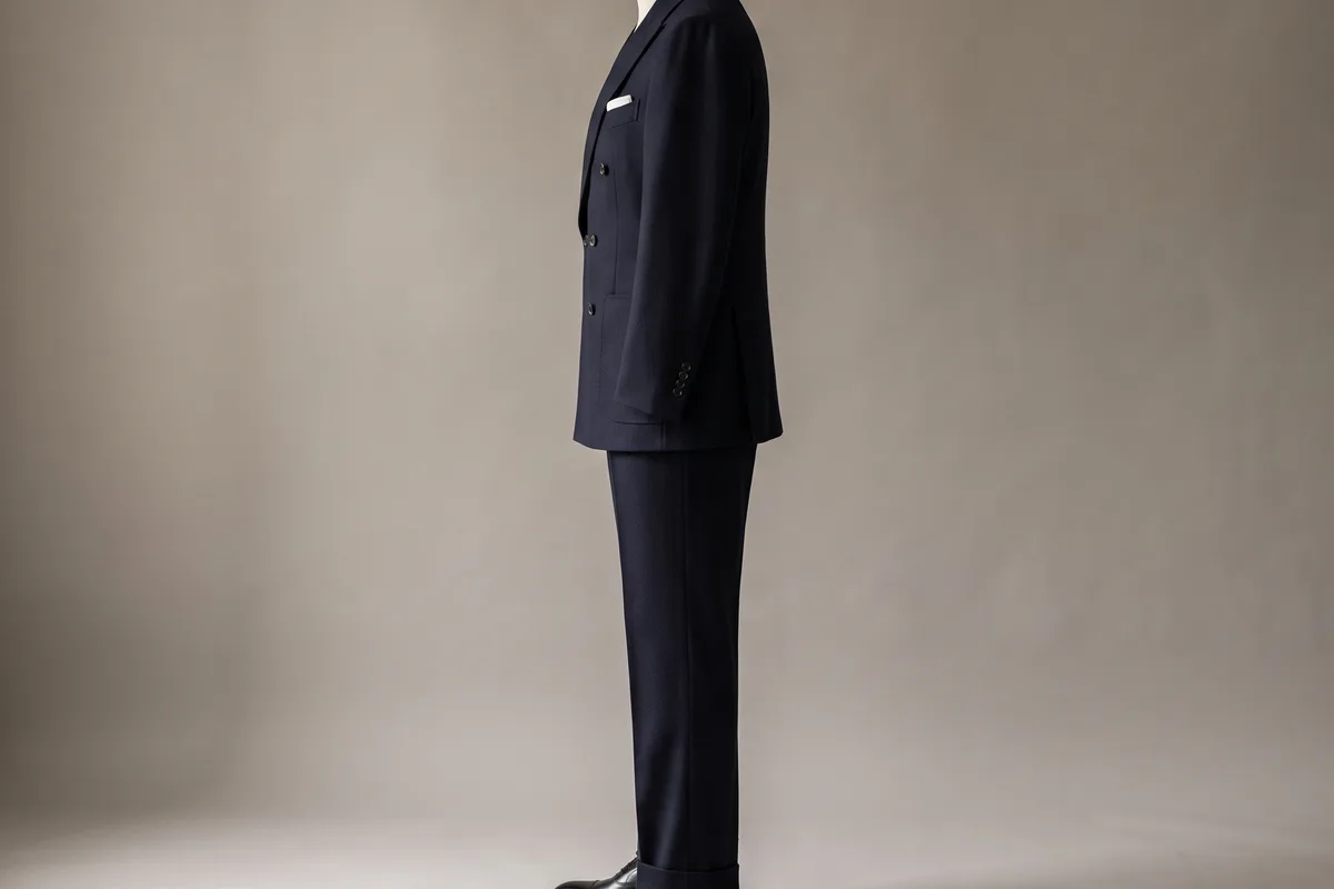 A double-breasted suit seen from the side, the jacket long enough to cover more than half the seat