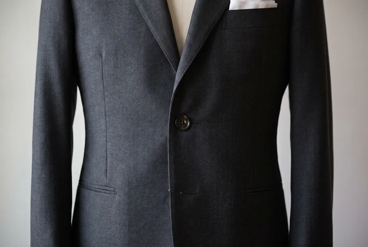 The front of a charcoal grey suit jacket fastened on the middle button, the cloth falling flat from chest to waist with no pull lines