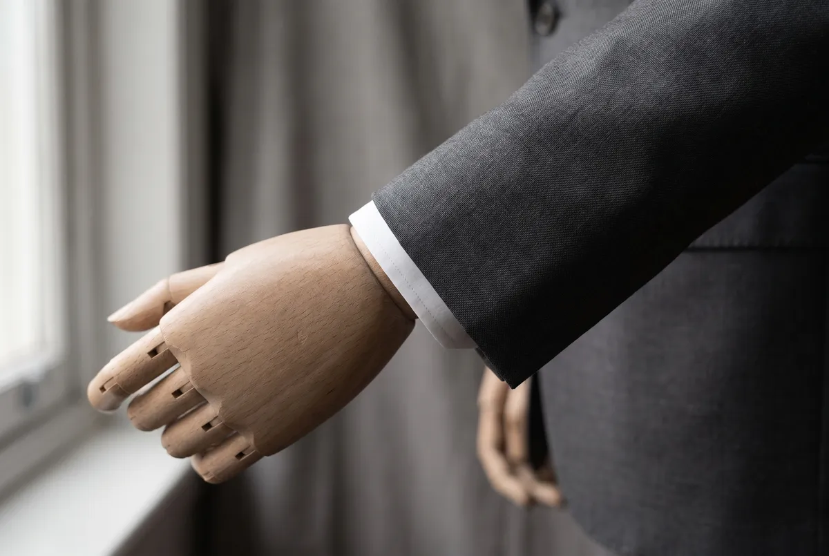 The cuff of a dress form with the arm reaching forward, a narrow margin of white shirt cuff showing beyond the jacket sleeve