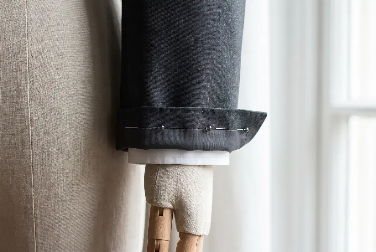 The cuff of a suit jacket on a dress form arm, pins set parallel to the sleeve edge to mark a shortening taken from the cuff